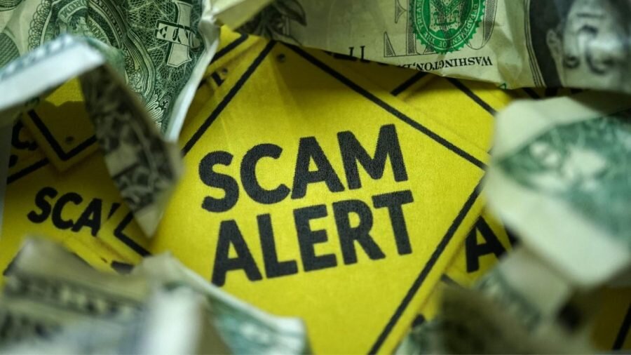 Yellow sign that reads "scam alert" with dollar bills surrounding the sign.